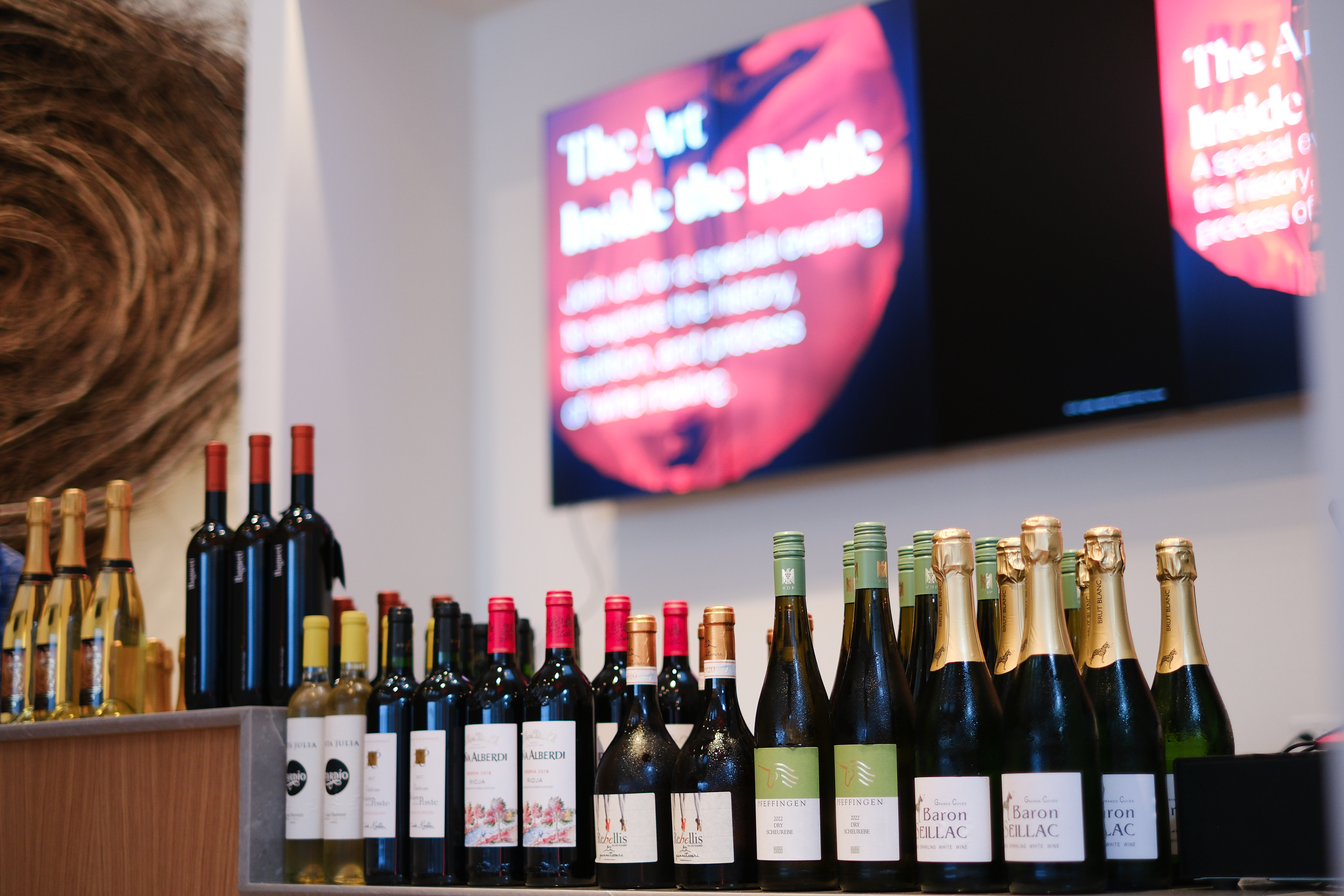 A lineup of wines on a counter, with a screen displaying "Art Inside the Bottle" in the background